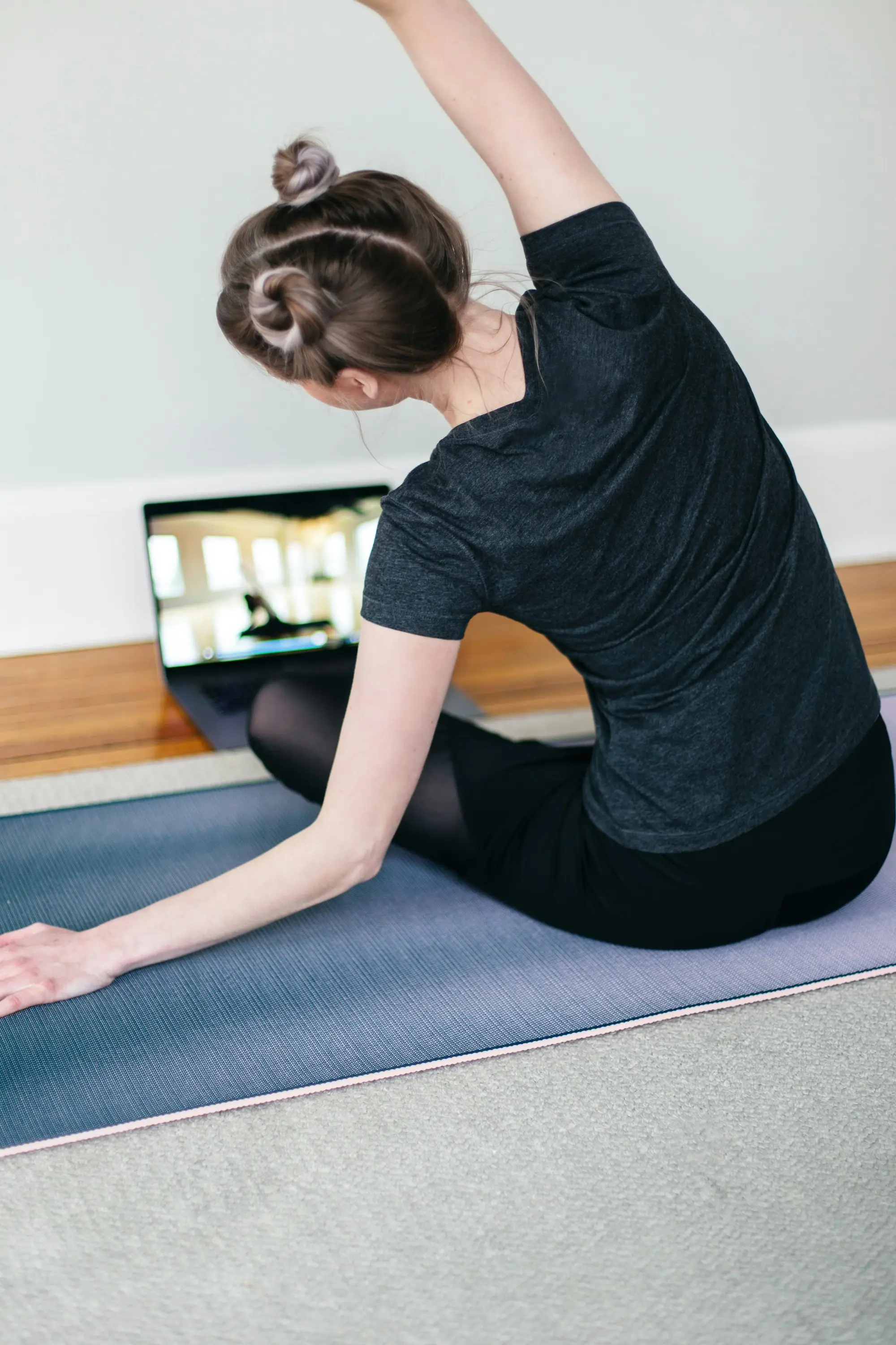 Une personne suit une séance d'étirements sur son ordinateur, assise sur un tapis dans son salon